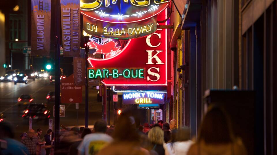 En neonskilte for 'Bar-B-Que' og 'Monkey Tonk Grill' på en travl gade om natten.