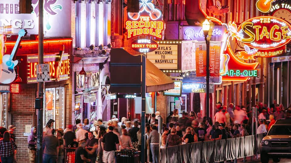 A crowded street with neon signs advertising music venues and restaurants.