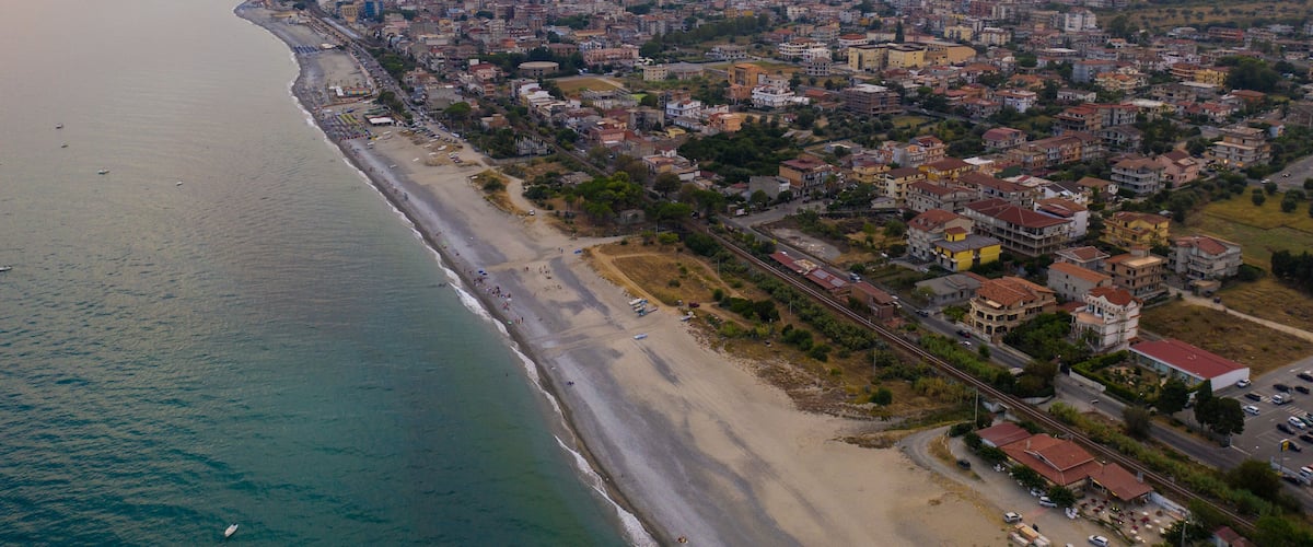 An aerial view of a coastal city with a beach, residential areas, and mountains in the background.
