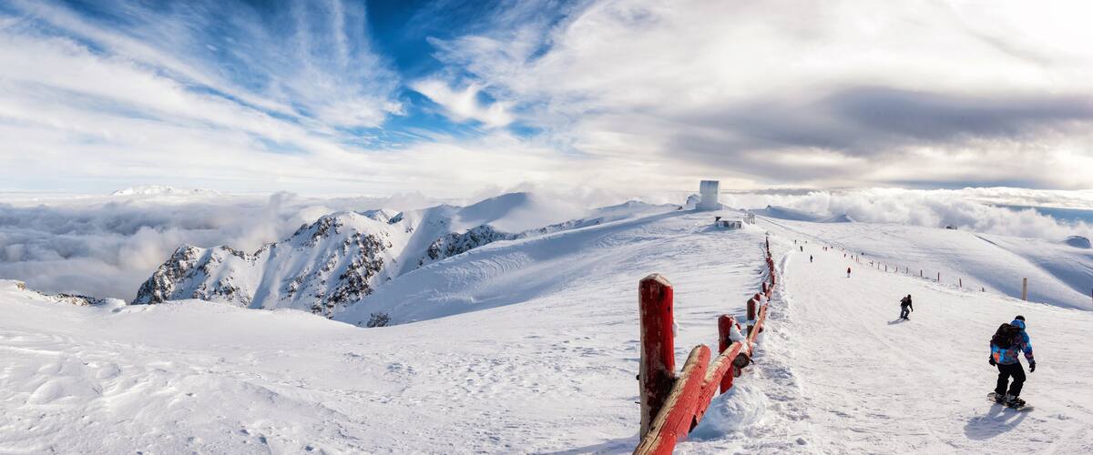 A snowy mountain landscape with a ski lift, snow-covered peaks, and a clear sky.
