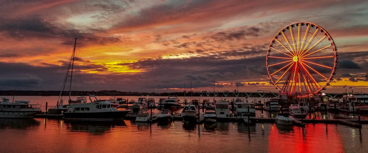 A sunset with a Ferris wheel and boats at a marina.