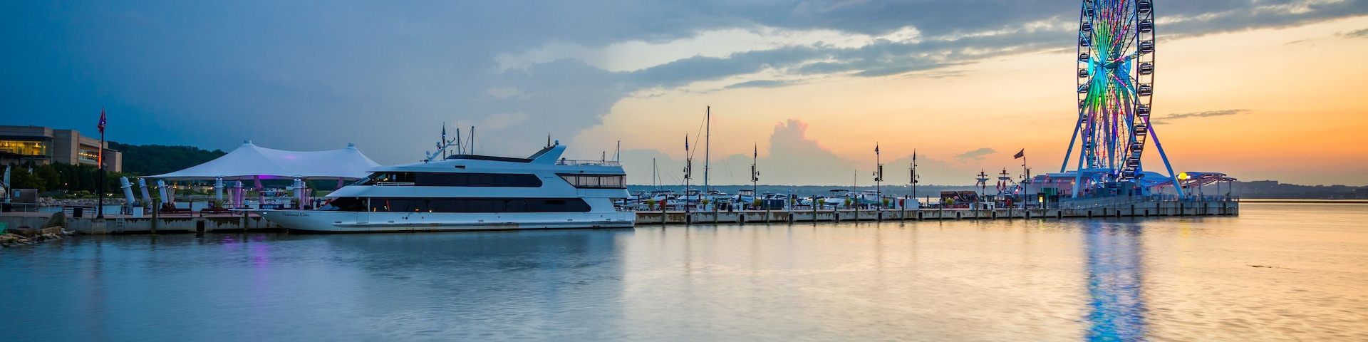 Una noria grande, un yate blanco y un muelle tranquilo al atardecer.