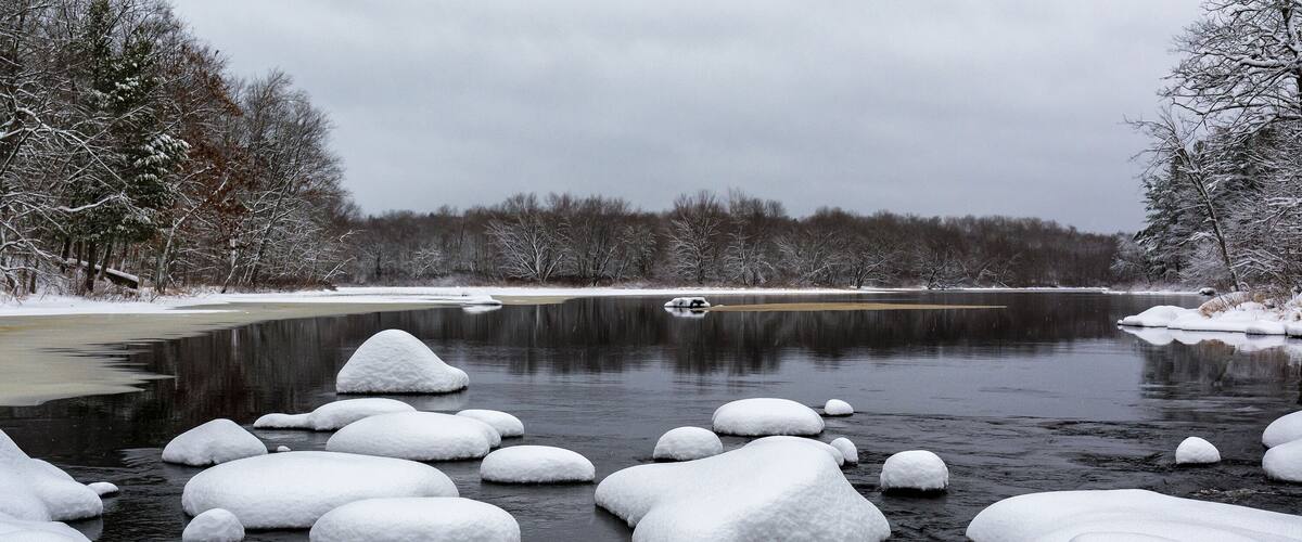A frozen river with snow-covered rocks and trees in a winter landscape.