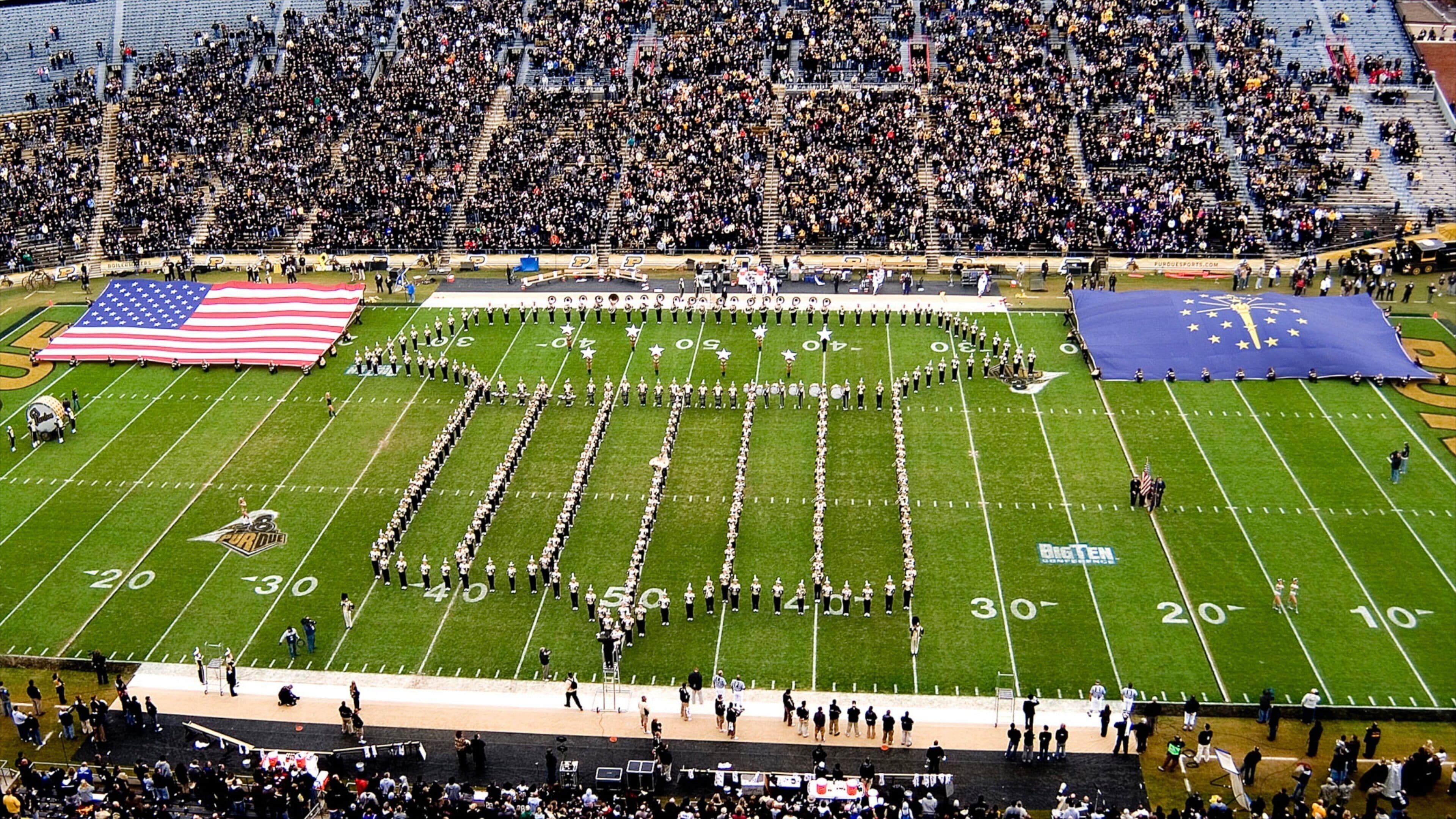 A football field with a marching band formation and a large crowd in the stands.