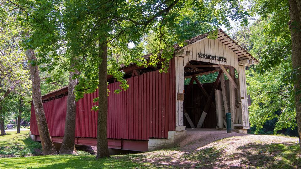 A covered bridge with a sign reading "Vermont 1875" in a wooded area.