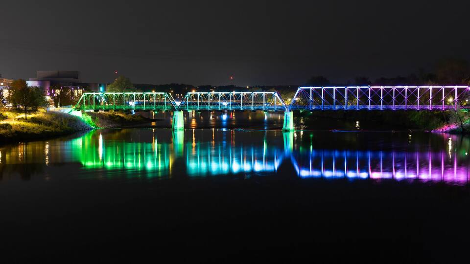 A brightly lit bridge with colorful lights reflecting on the water at night.