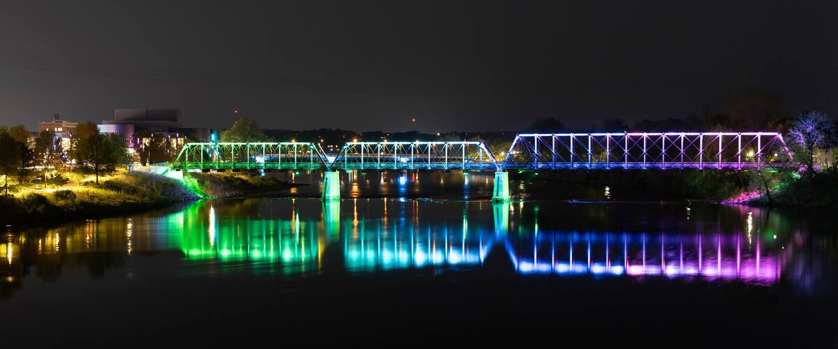A brightly lit bridge with colorful lights reflecting on the water at night.