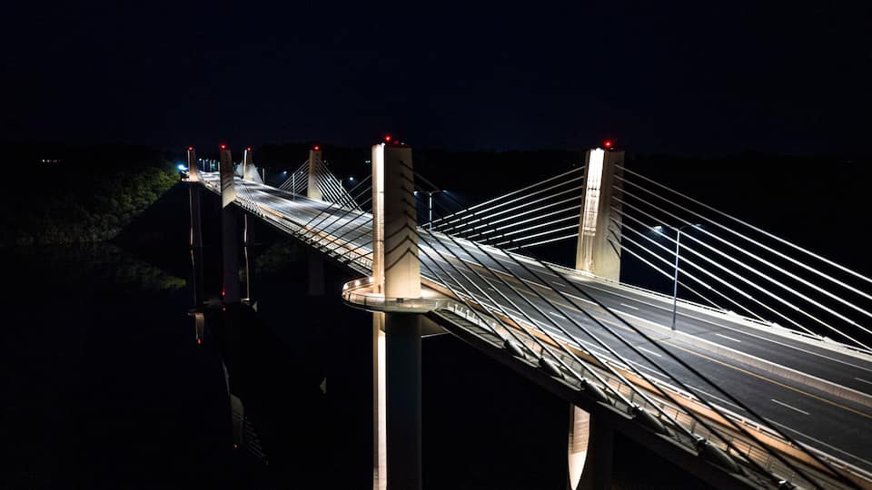 A nighttime view of a long suspension bridge with illuminated cables and towers.