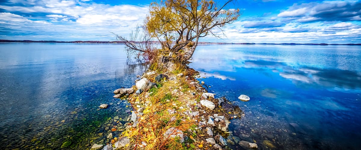 A clear lake with a rocky shoreline and a solitary tree.