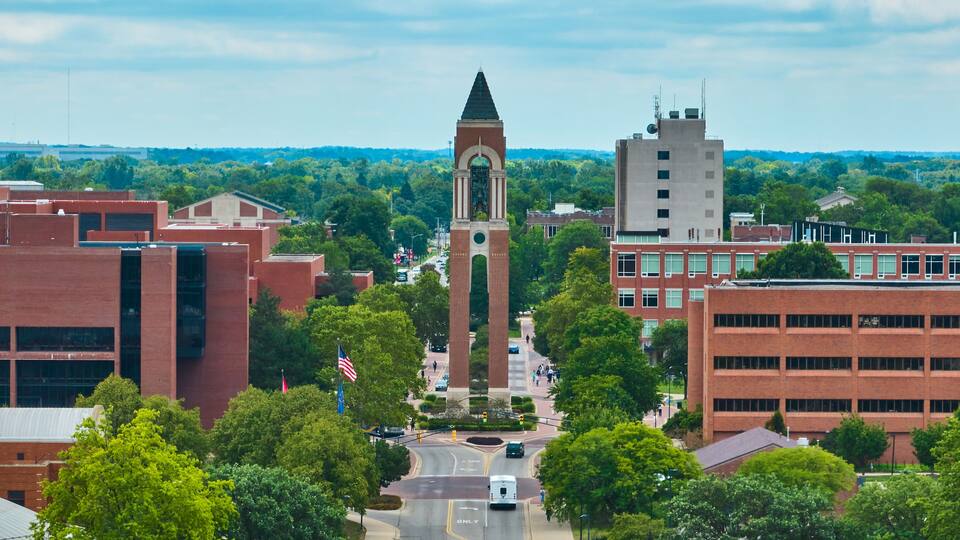 A campus with a prominent clock tower, surrounded by modern buildings and lush greenery.