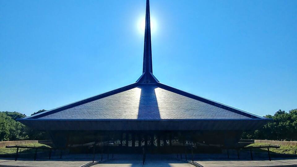 A modern building with a pointed roof and a cross at the top, set against a clear blue sky.