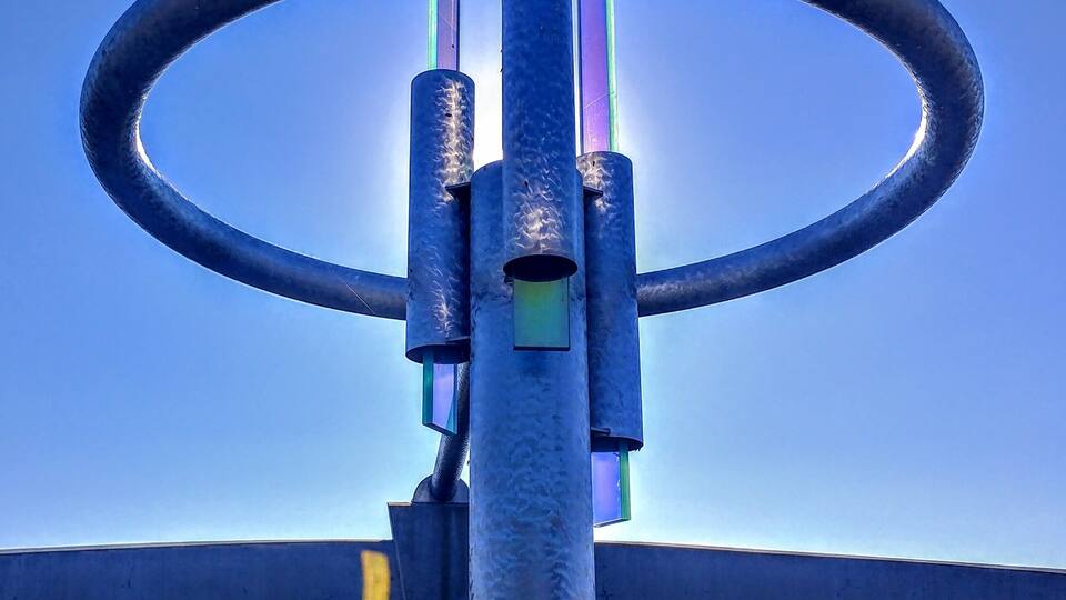 A sculpture with a large circular ring and vertical elements, set against a blue sky.
