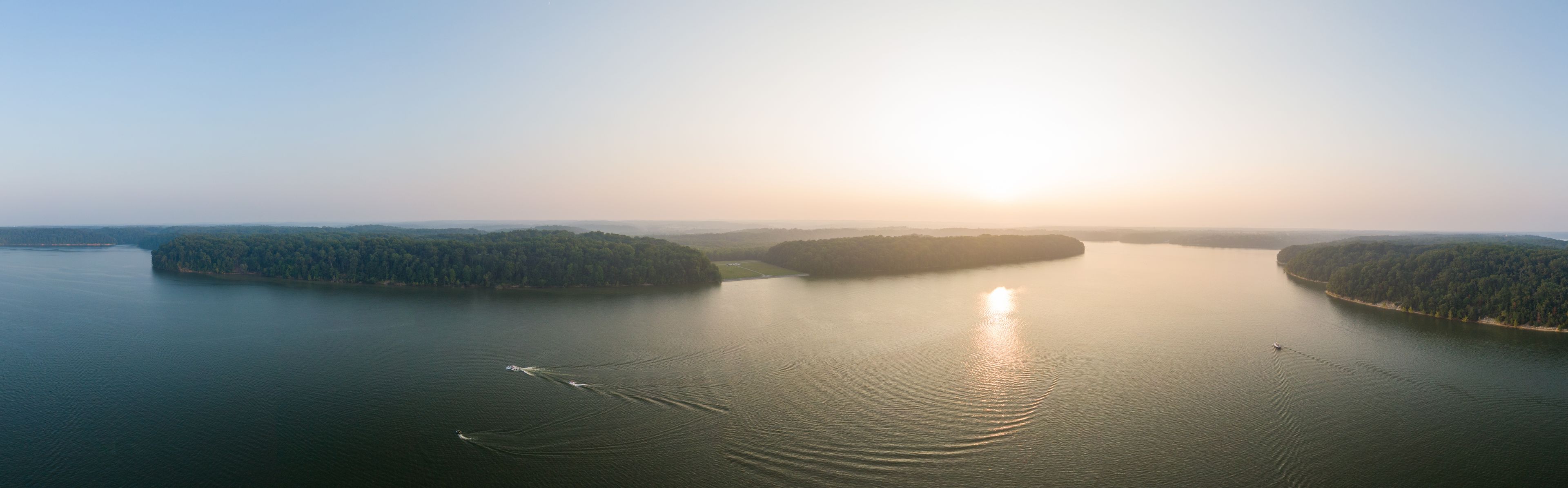 A calm lake surrounded by forested islands with a boat creating ripples on the water.