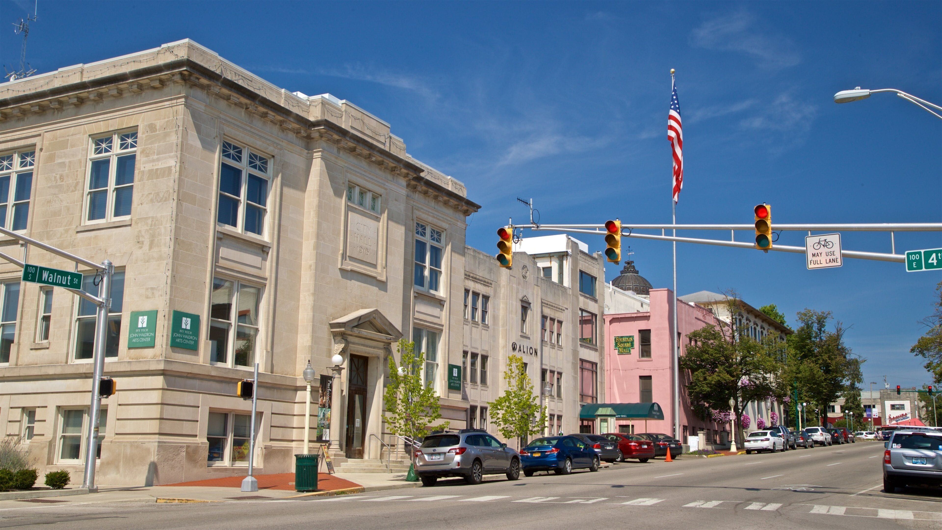 A street with buildings, cars, traffic lights, and an American flag.