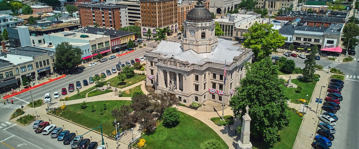 A cityscape with a prominent historic building with a dome and columns, surrounded by modern buildings and a parking lot.
