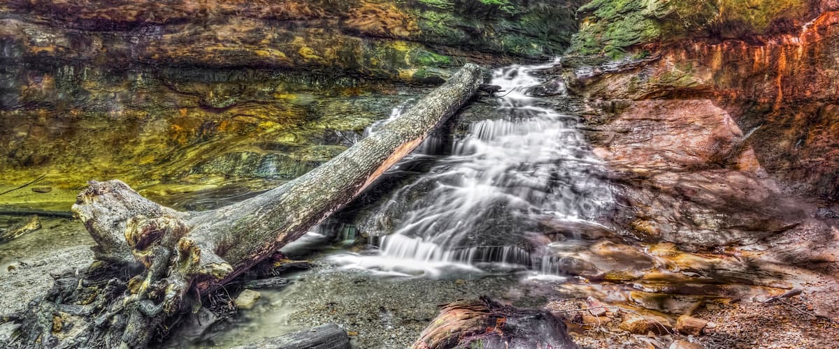 Water cascades over colorful sandstone from a narrow passage with green rocky walls In Indiana's Turkey Run State Park.