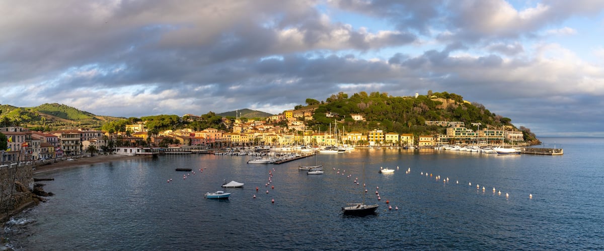 A coastal town with a hilltop castle, boats in the harbor, and colorful buildings along the waterfront.