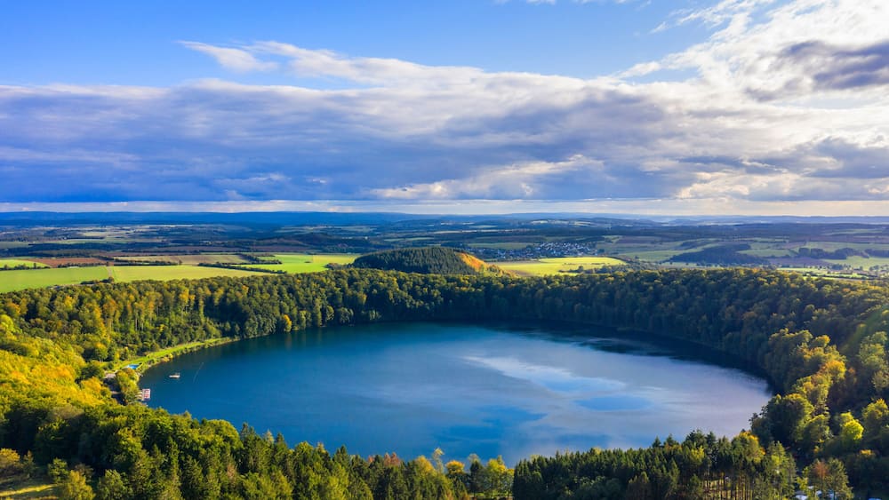 A lake surrounded by dense forest and rolling hills under a partly cloudy sky.
