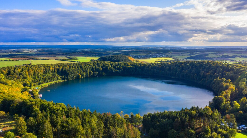 A lake surrounded by dense forest and rolling hills under a partly cloudy sky.