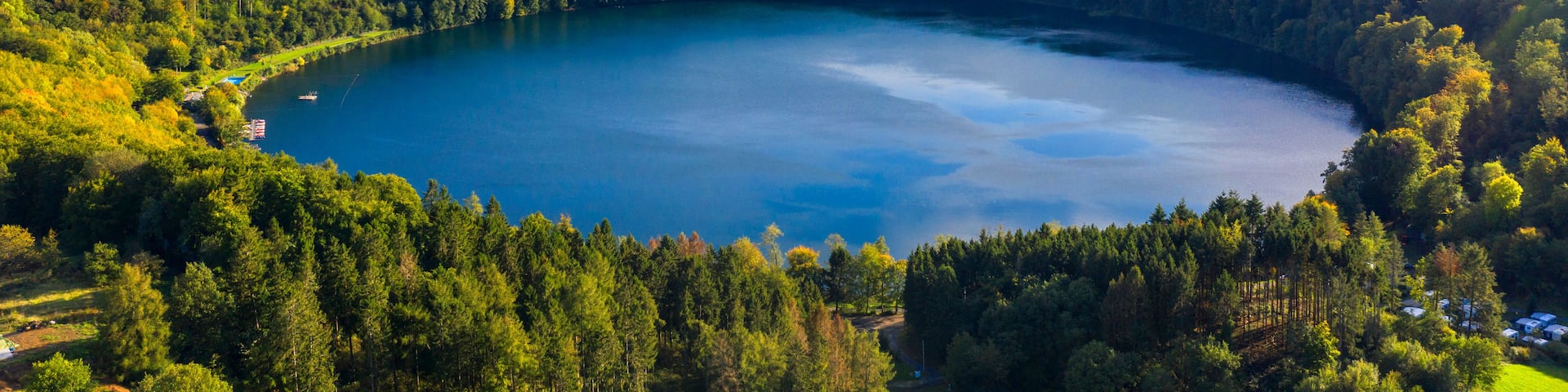 A lake surrounded by dense forest and rolling hills under a partly cloudy sky.