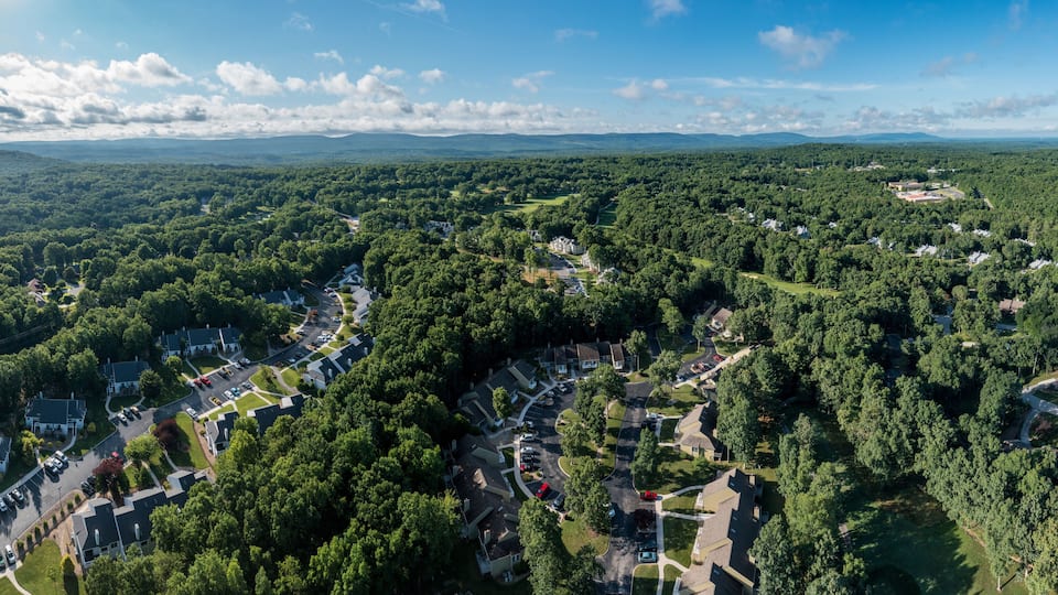 An aerial view of a residential area with houses, roads, and surrounding forested landscape.