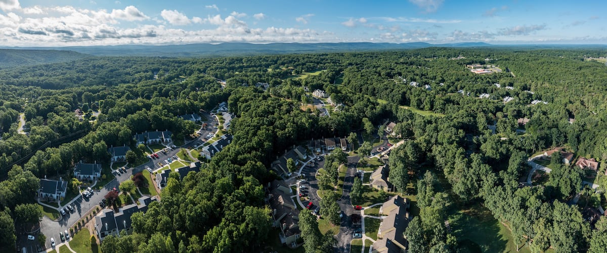 An aerial view of a residential area with houses, roads, and surrounding forested landscape.