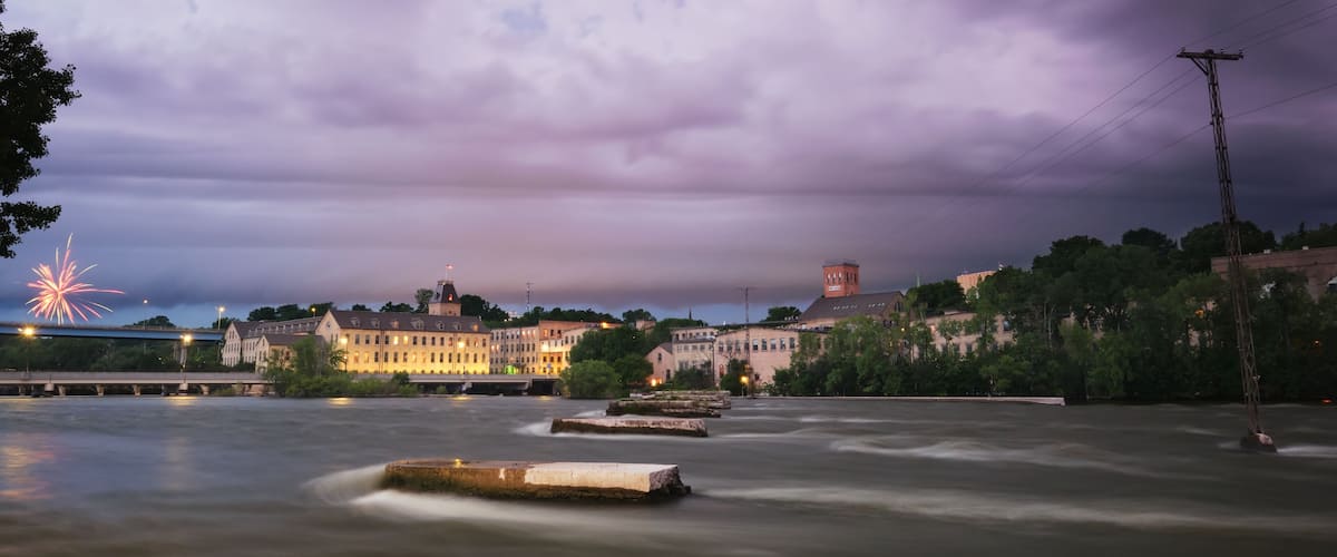 A river with a bridge, buildings, and fireworks in the background.