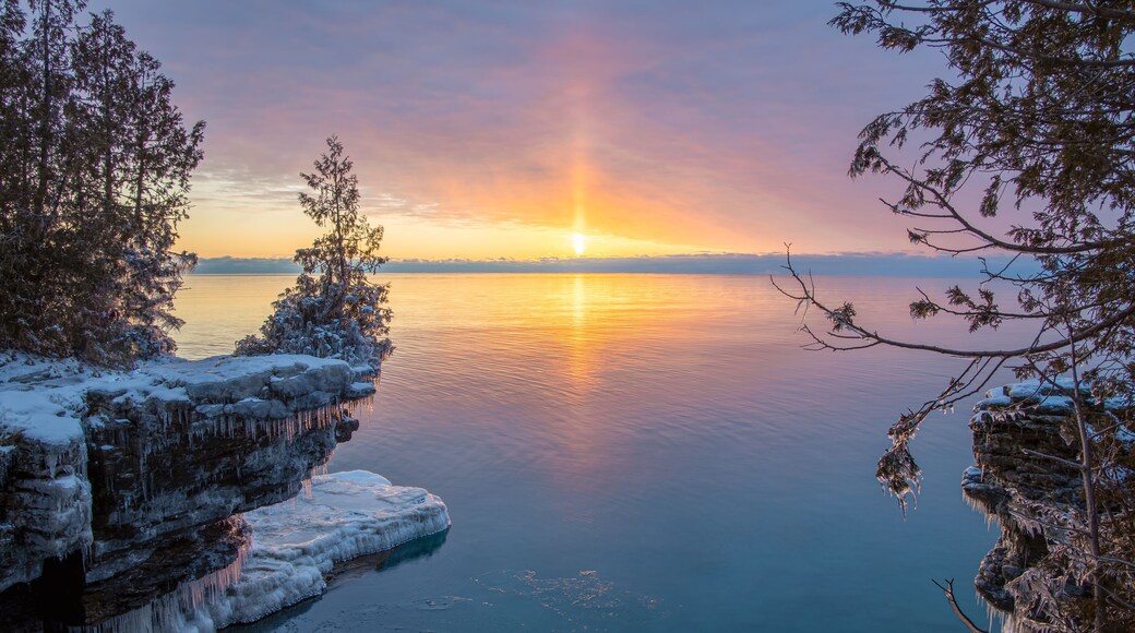 Un lago helado con estalactitas, un atardecer y árboles cubiertos de nieve.