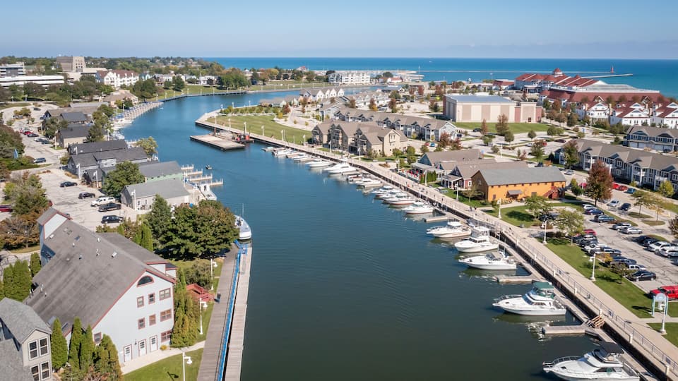 A marina with boats docked along a waterfront, surrounded by residential buildings and a clear blue sky.