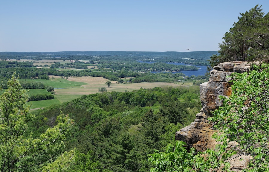 A mountainous landscape with a lake, dense forest, and a rocky outcrop.