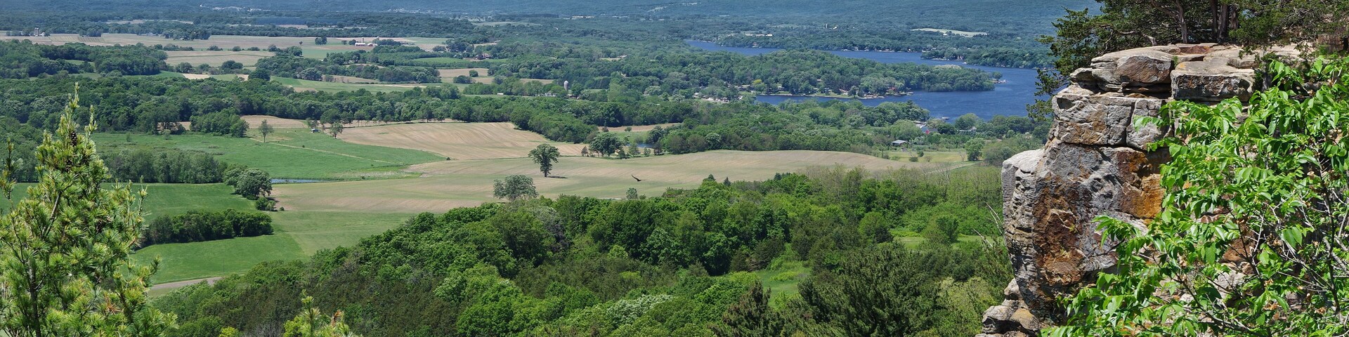 A mountainous landscape with a lake, dense forest, and a rocky outcrop.