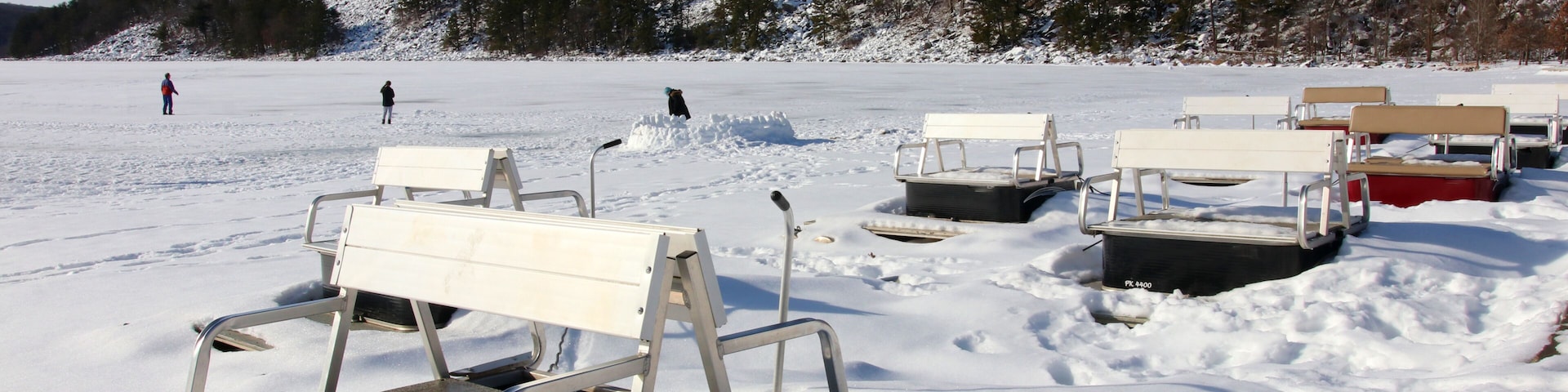 Um lago congelado com bancos cobertos de neve e pessoas ao longe.
