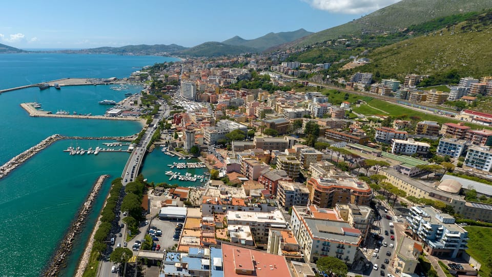 A coastal city with a marina, dense urban buildings, and a mountainous backdrop.