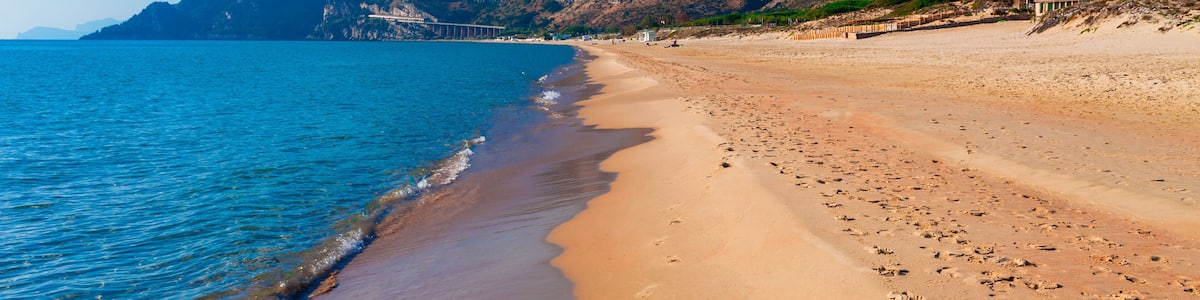 A beach with clear blue water, a sandy shore, and rocky cliffs in the background.