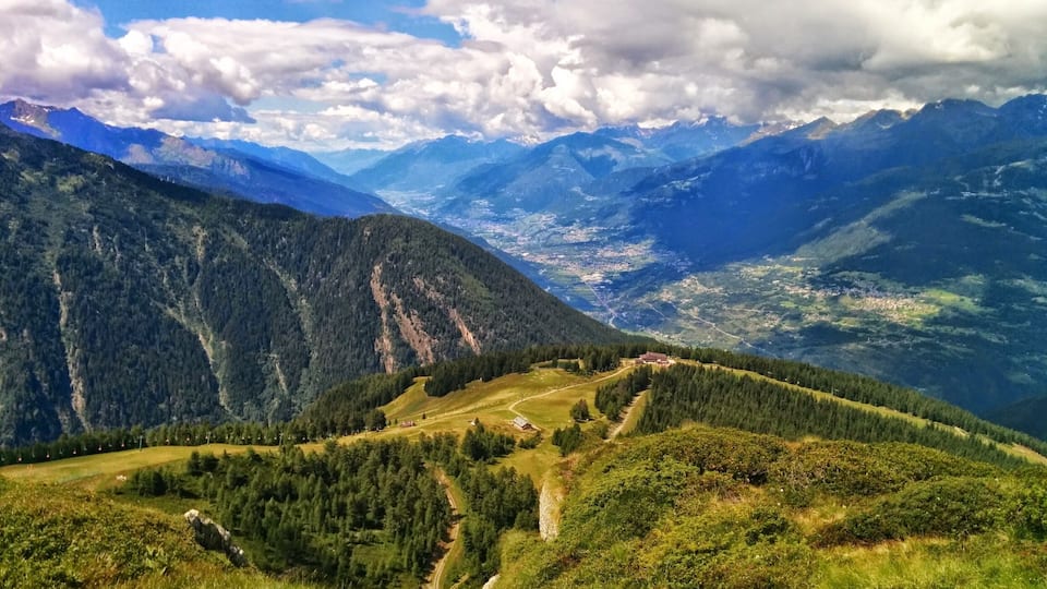 A mountainous landscape with a valley, forested areas, and a distant town.