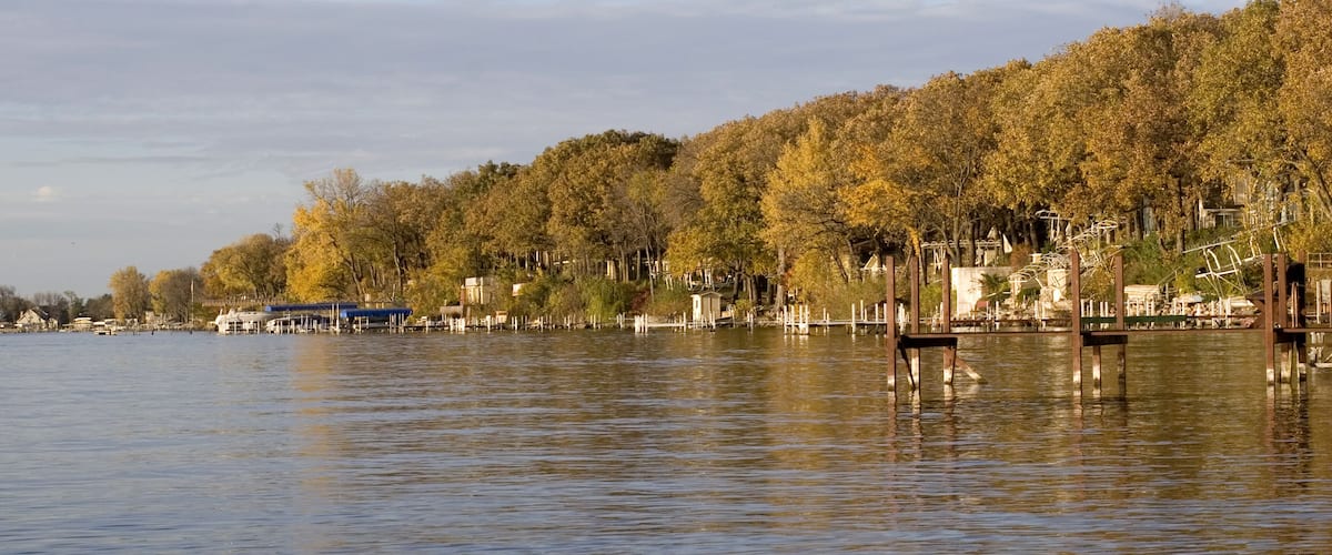 A calm lake with a forested shoreline and a pier extending into the water.