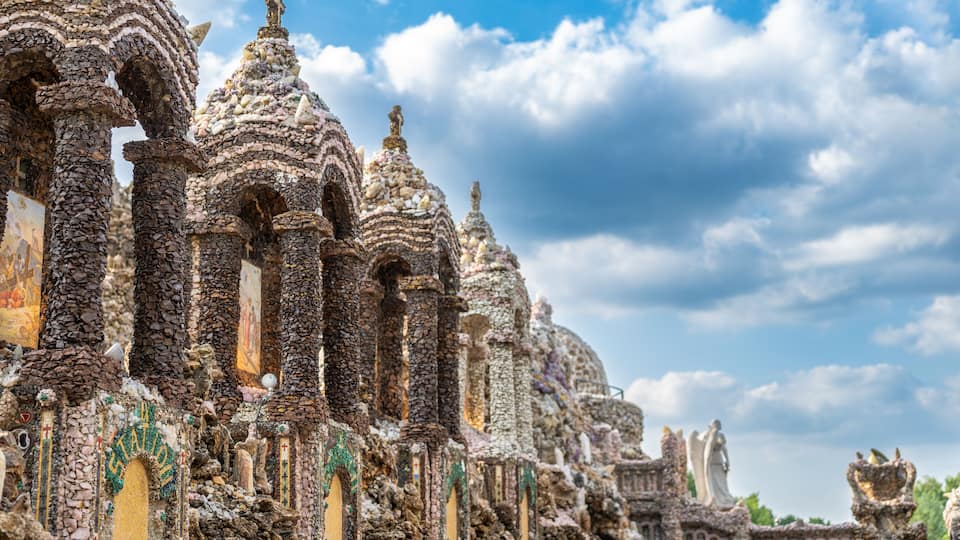 A historic stone structure with intricate carvings and domes, set against a partly cloudy sky.
