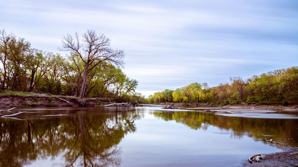 A calm river reflecting trees and a clear sky.