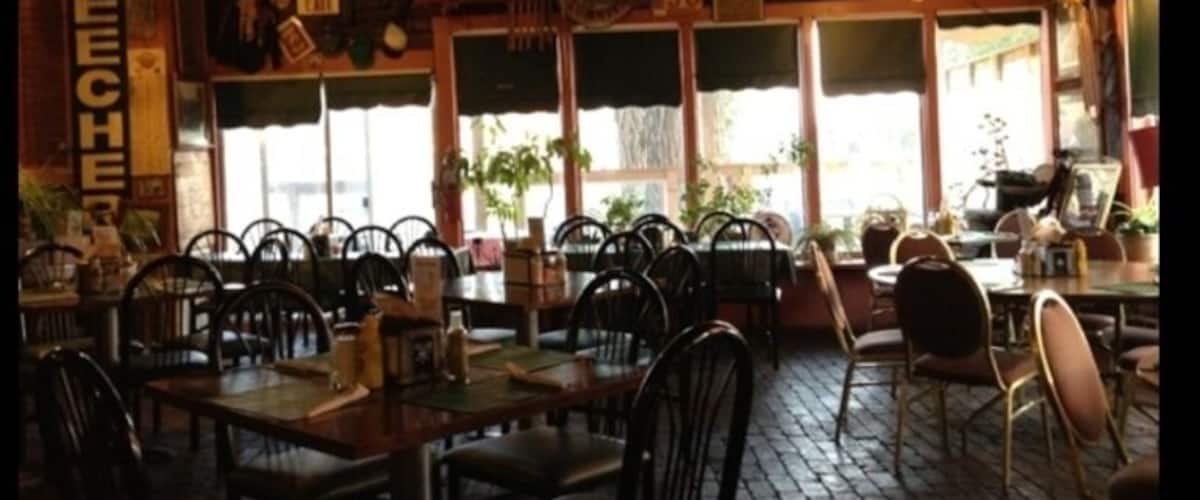 A rustic wooden interior with tables and chairs, large windows, and various decorations.