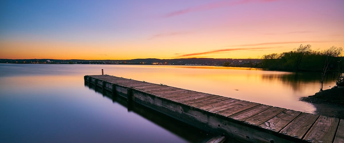 A wooden pier extending into calm water at sunset.