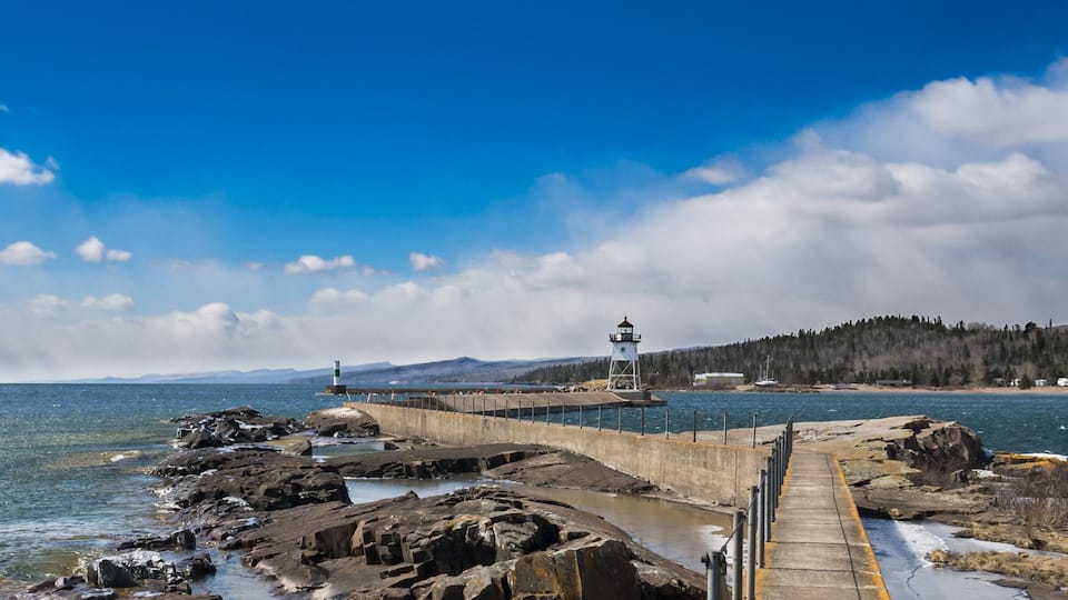 A rocky shoreline with a pier leading to a lighthouse.