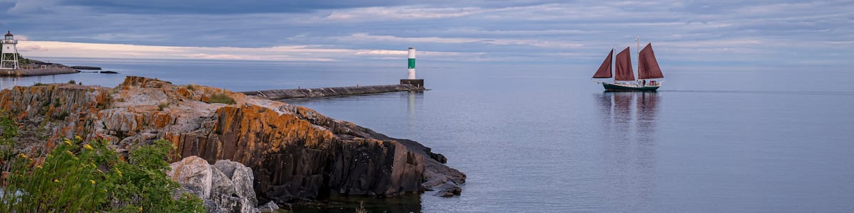 Une côte rocheuse, avec un phare et un voilier sur l’eau.