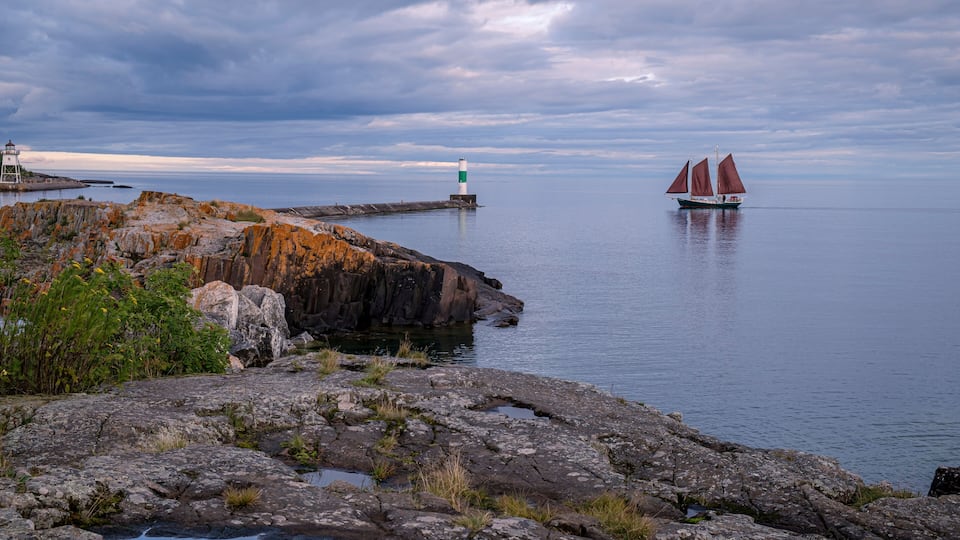 A rocky coastline with a lighthouse and a sailboat on the water.