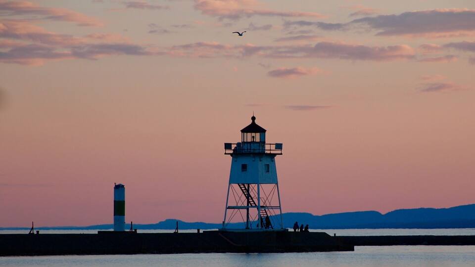 A lighthouse at sunset with a seagull flying in the sky.