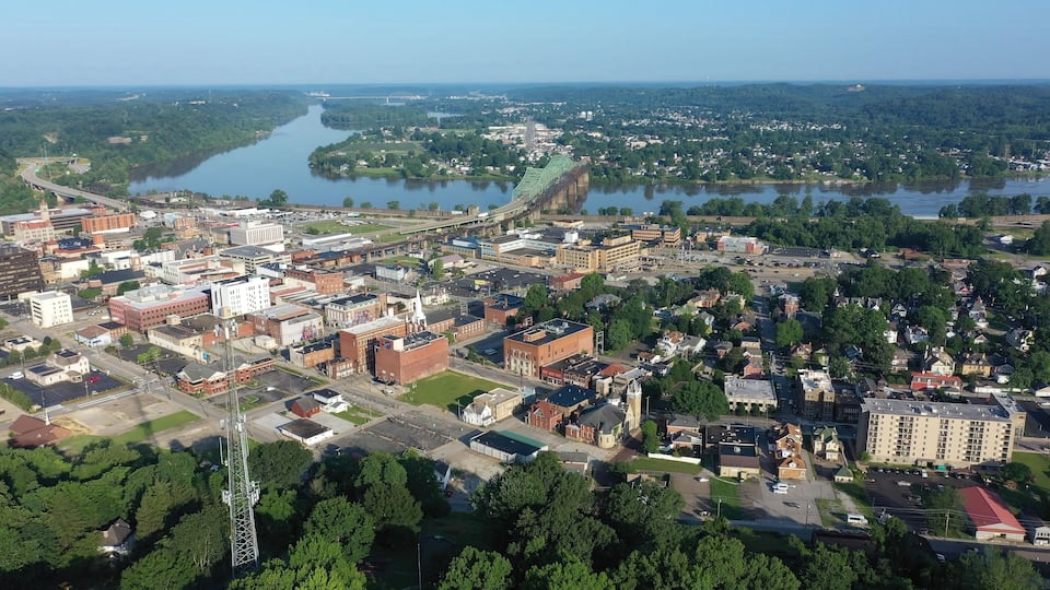 An aerial view of a city with a river, a bridge, and surrounding greenery.