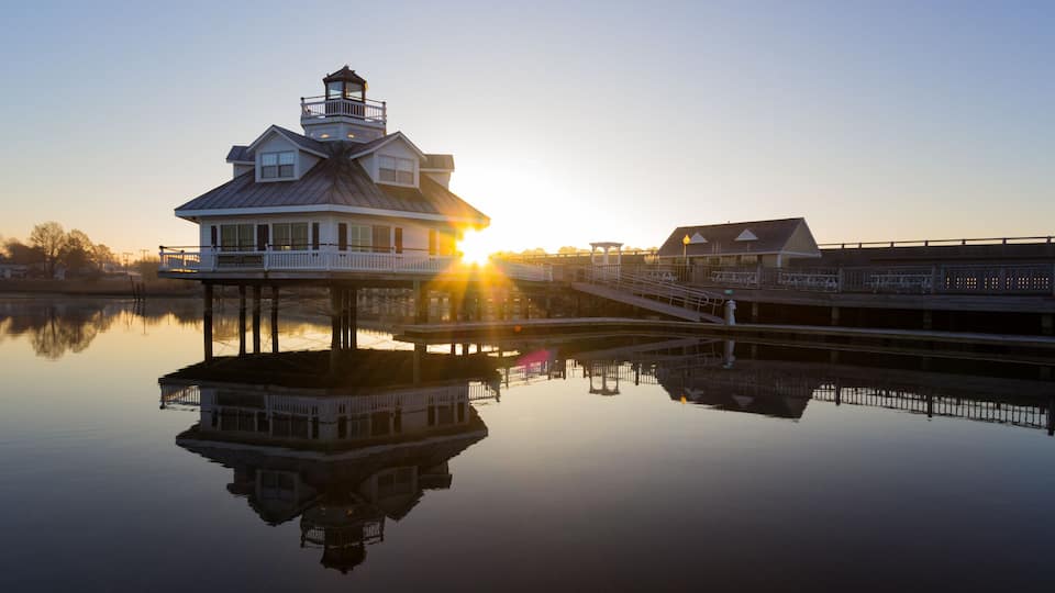 A waterfront house with a balcony, a pier, and a reflection in the water.