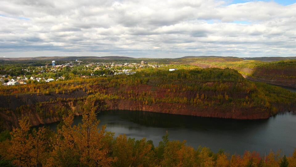 A river surrounded by autumn foliage, a town in the background, and a cloudy sky.