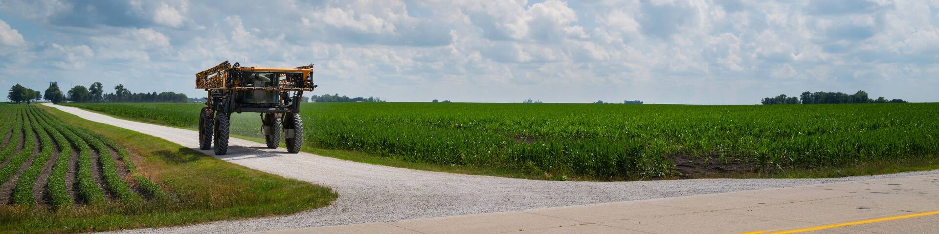 Dramatic cloudscape over the Midwest American road with a tractor traveling through cornfields in Iowa. American Heartland landscape photography.