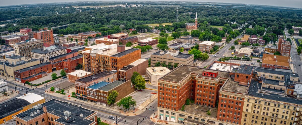 An aerial view of a city with a prominent red-brick building, a green park, and a distant church steeple.