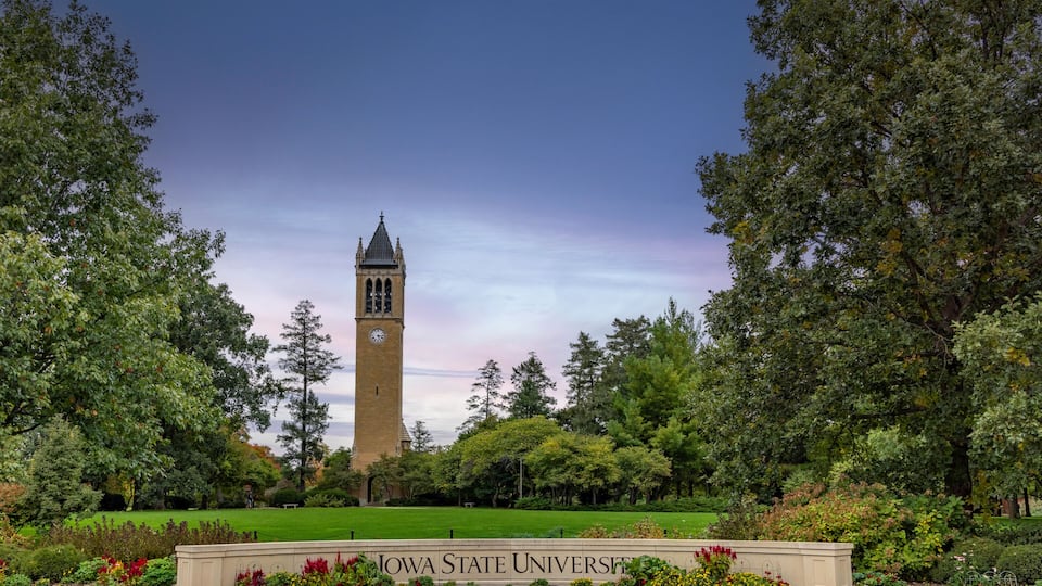 A clock tower, lush greenery, and the Iowa State University sign.